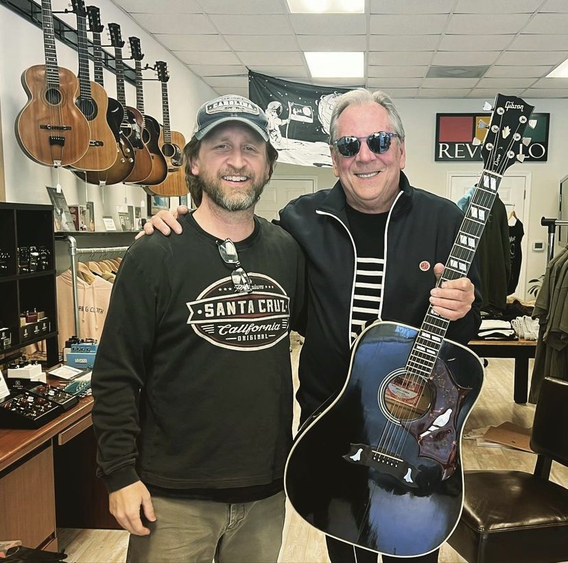 two men posing with a Gibson Dove acoustic guitar